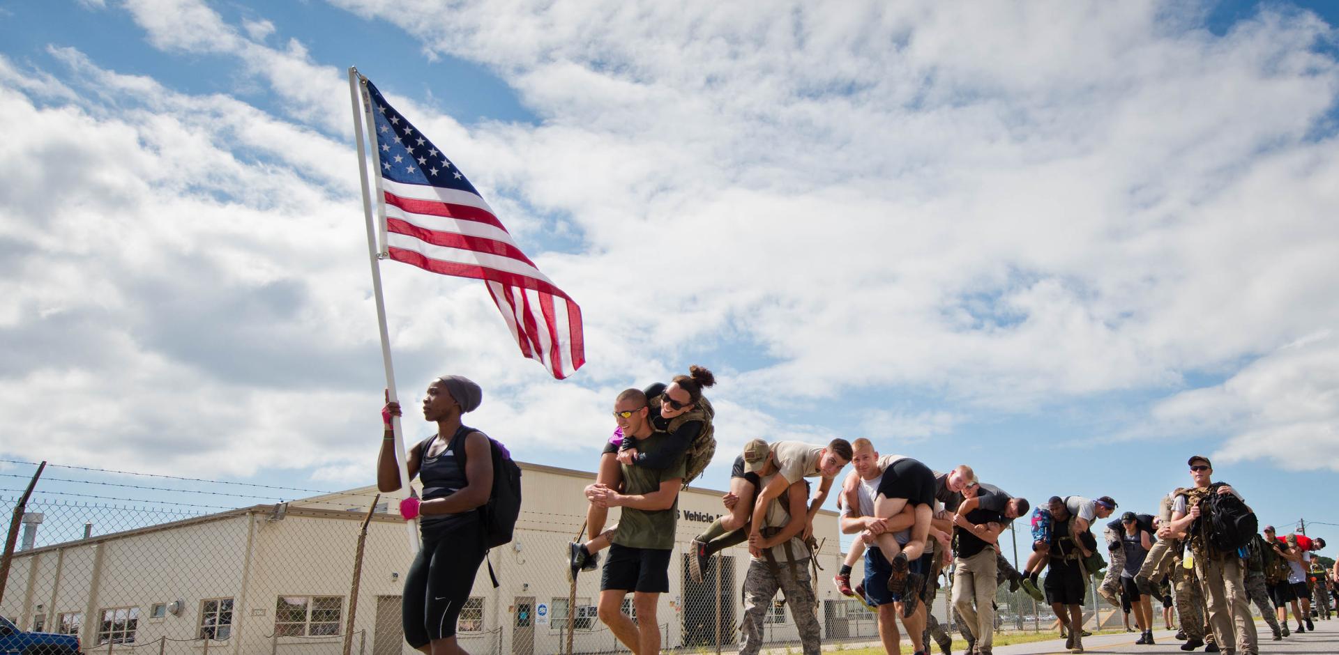 Participants march past the vehicle maintenance facility carrying simulated wounded personnel
